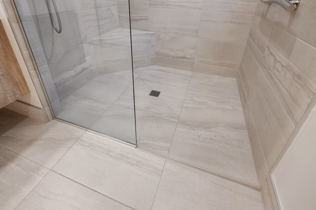 Curbless tiled shower with a fixed glass panel, large-format floor tile sloped to a square center drain